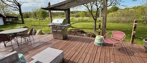 A wooden deck with a grill, wicker furniture, and a pergola.