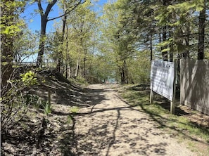 Ein unbefestigter Weg führt zu einem Strandabschnitt, an dem eine Schanze die Strandzeiten und Regeln für den öffentlichen Zugang anzeigt.
