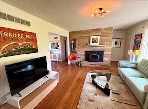 Ein Wohnzimmer mit Flachbildfernseher, Kamin, einer Couch und einem Essbereich mit einem roten Sessel.