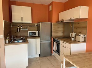 Eine kompakte Küche mit weißen Schränken, einem Edelstahlkühlschrank, einer Mikrowelle, einem Toaster und einem Spülbecken.