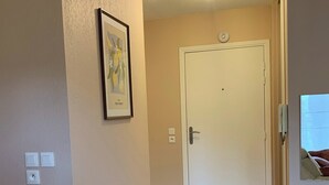 A hallway with a white door, a framed picture on the wall, and two small stools. - Cosy apartment with pool near the center (Draguignan)