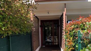 A narrow pathway leading to a building entrance with a wooden facade and a green metal fence on one side.