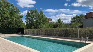 A rectangular swimming pool with a wooden deck surrounding it, a metal fence, and trees in the background. - Cosy apartment with pool near the center (Draguignan)