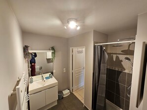Un baño con lavamanos blanco, espejo, ducha y una lámpara en el techo.