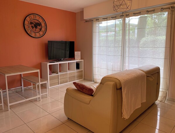 Una sala de estar con un sofá, televisor, mueble blanco y una ventana con cortinas.