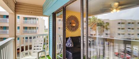 Un balcon avec un fauteuil à bascule blanc, un canapé noir et un élément de décoration murale en forme de soleil rayonnant.