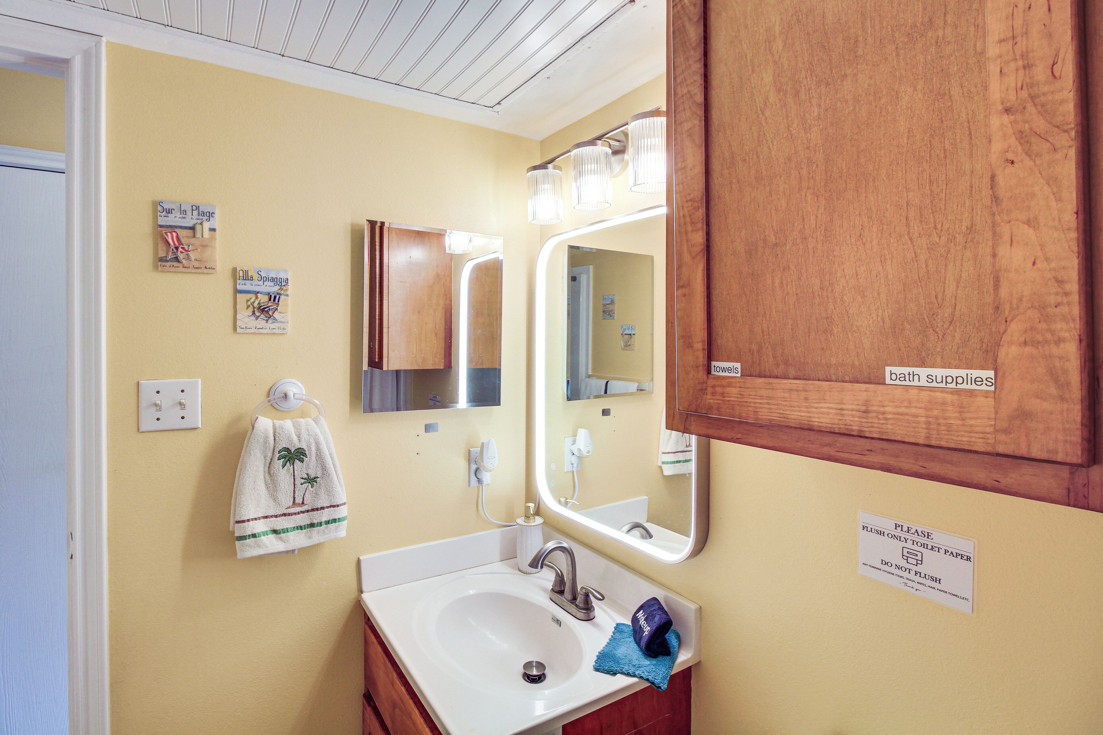 A bathroom with a sink, mirror, towel rack, and a sign instructing to flush only toilet paper.