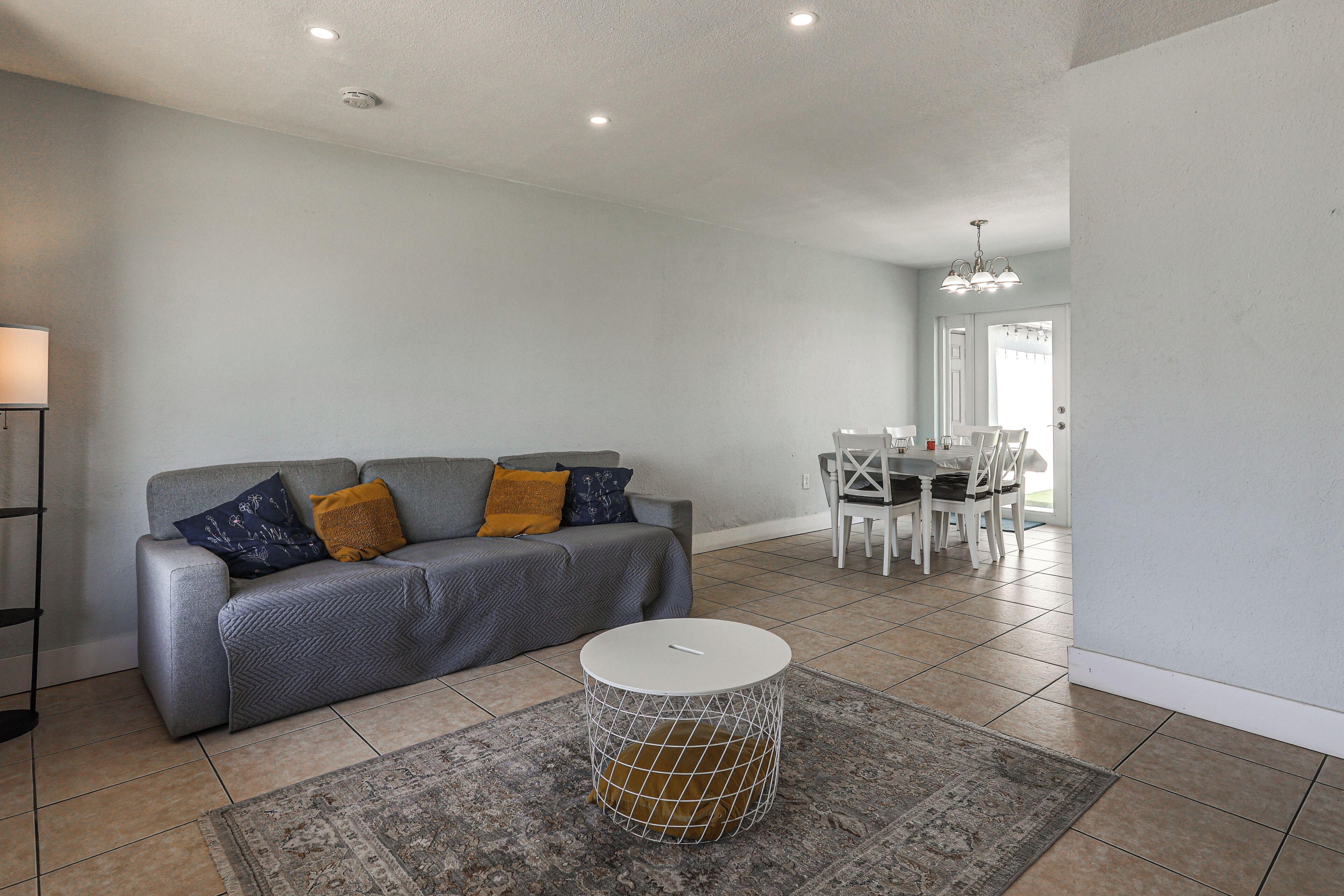 A living room with a grey sofa, a round coffee table, and a dining area with a white table and chairs.