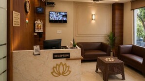 A reception area with a marble counter, a ceiling fan, a television, and a reception desk. - Hotel Lotus Palace (Lucknow)