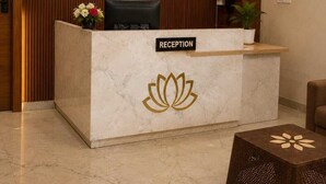 A reception desk with a clock, a television, and a sign indicating check-in and check-out times. - Hotel Lotus Palace (Lucknow)