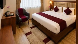 A hotel room with a large bed, a desk, a chair, a TV, a ceiling fan, and a window with curtains. - Hotel Lotus Palace (Lucknow)