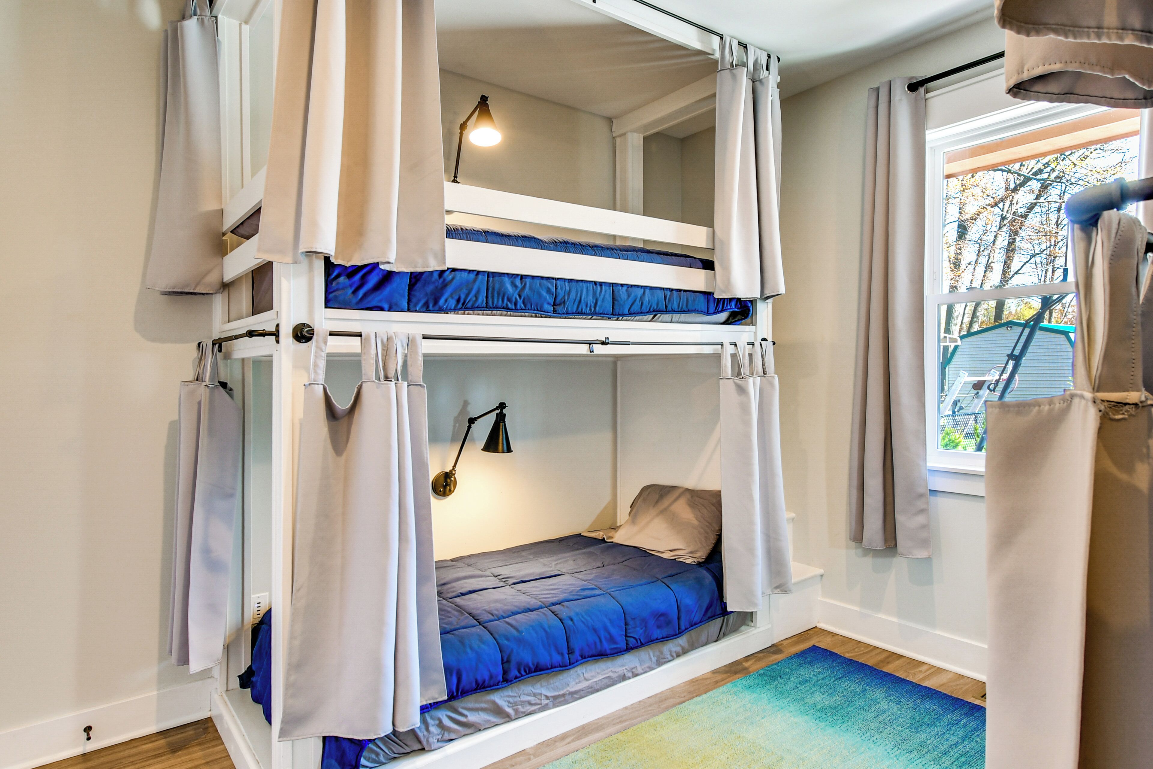 A bunk bed room with curtains, a window, and a lamp.