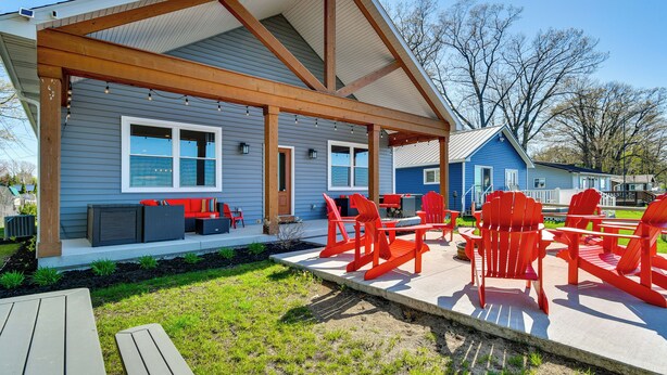 A covered patio area with outdoor seating, a wooden pergola, and a view of a blue house in the background. - Houghton Lake Getaway: Dock, Foosball & Yard! (Houghton Lake)