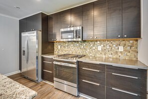 Eine moderne Küche mit Edelstahlgeräten, dunklen Holzausziehtüren und einer Mosaik-Bodenfliese als Rückwand.