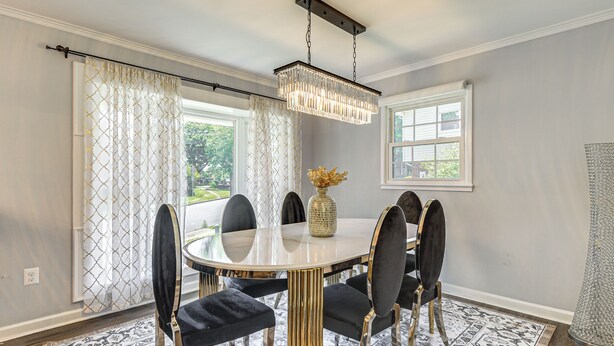 A dining room with a round table, black upholstered chairs, a chandelier, and patterned curtains. - Easy Hwy Trip to DC! Group Retreat w/ Yard (Woodbridge)