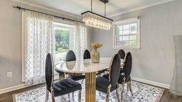 A dining room with a round table, black upholstered chairs, a chandelier, and patterned curtains.