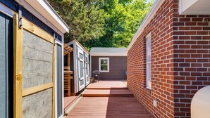 Une étroite terrasse en bois mène à un bâtiment en briques doté d’une fenêtre et d’une porte.