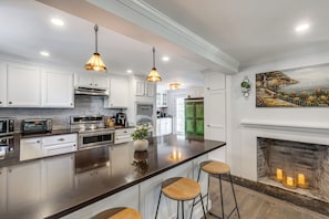 A modern kitchen with white cabinets, a large island, stainless steel appliances, and a fireplace.