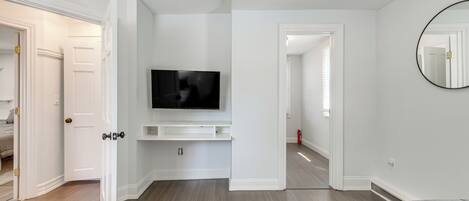 Une chambre moderne dotée d’un téléviseur à écran plat fixé au mur, d’un grand miroir et d’une porte donnant sur une autre pièce.