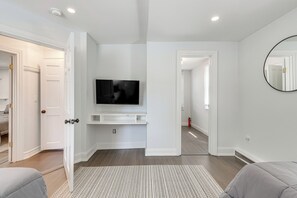 A modern room with a flat-screen TV mounted on the wall, a large mirror, and a door leading to another room.