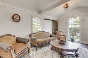 Ein Zimmer mit großem Fenster, einer Couch, einem Sessel, einem Tisch und einer Wanduhr.