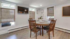 Une salle à manger avec une table ronde, six chaises et une fenêtre avec des stores.