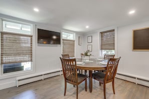 A dining room with a round table, six chairs, and a window with blinds.