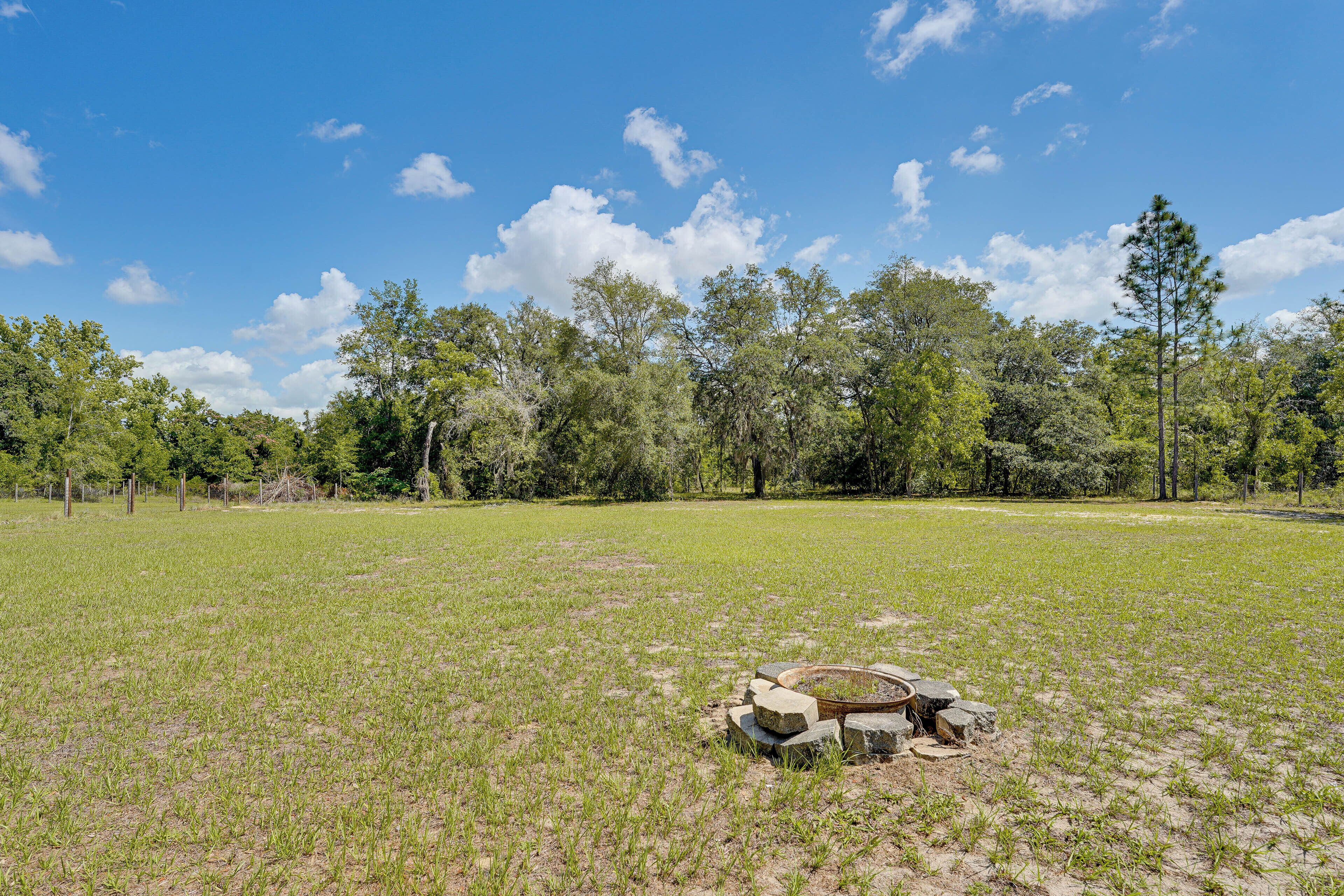 A grassy field with a fire pit and trees in the background.