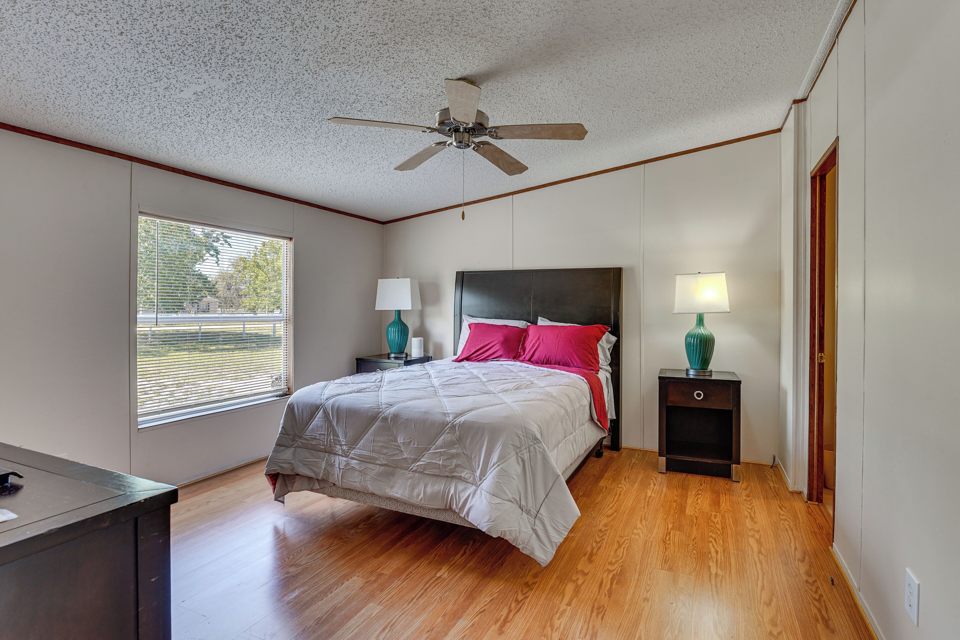 Une chambre à coucher comprenant un lit, deux tables de chevet, un ventilateur de plafond, une fenêtre et un bureau.