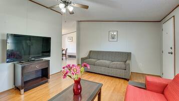 A living room with a flat-screen TV, a red vase with flowers, a grey sofa, and a ceiling fan.