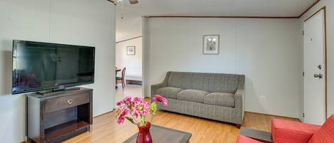 Een woonkamer met een flatscreen televisie, een rode vaas met bloemen, een grijze bank en een plafondventilator.