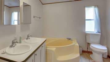 A bathroom with two sinks, a bathtub, a toilet, and a window with a curtain.