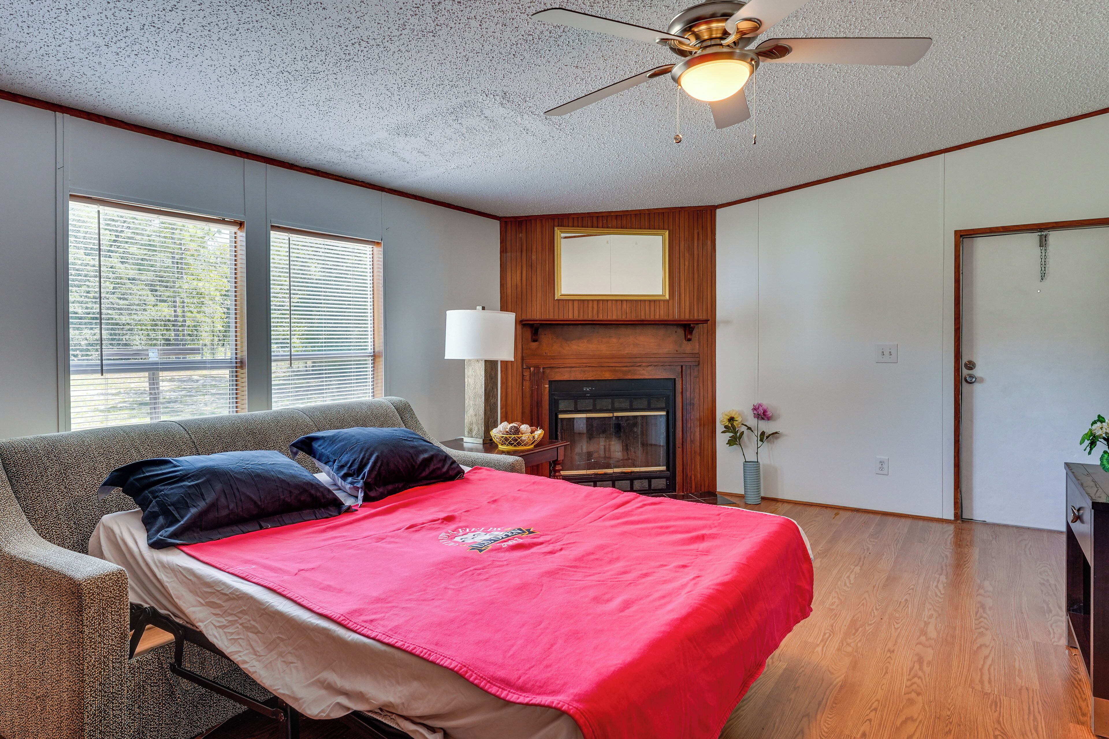 Une chambre à coucher avec un lit, un ventilateur de plafond, une cheminée et une fenêtre avec des stores.