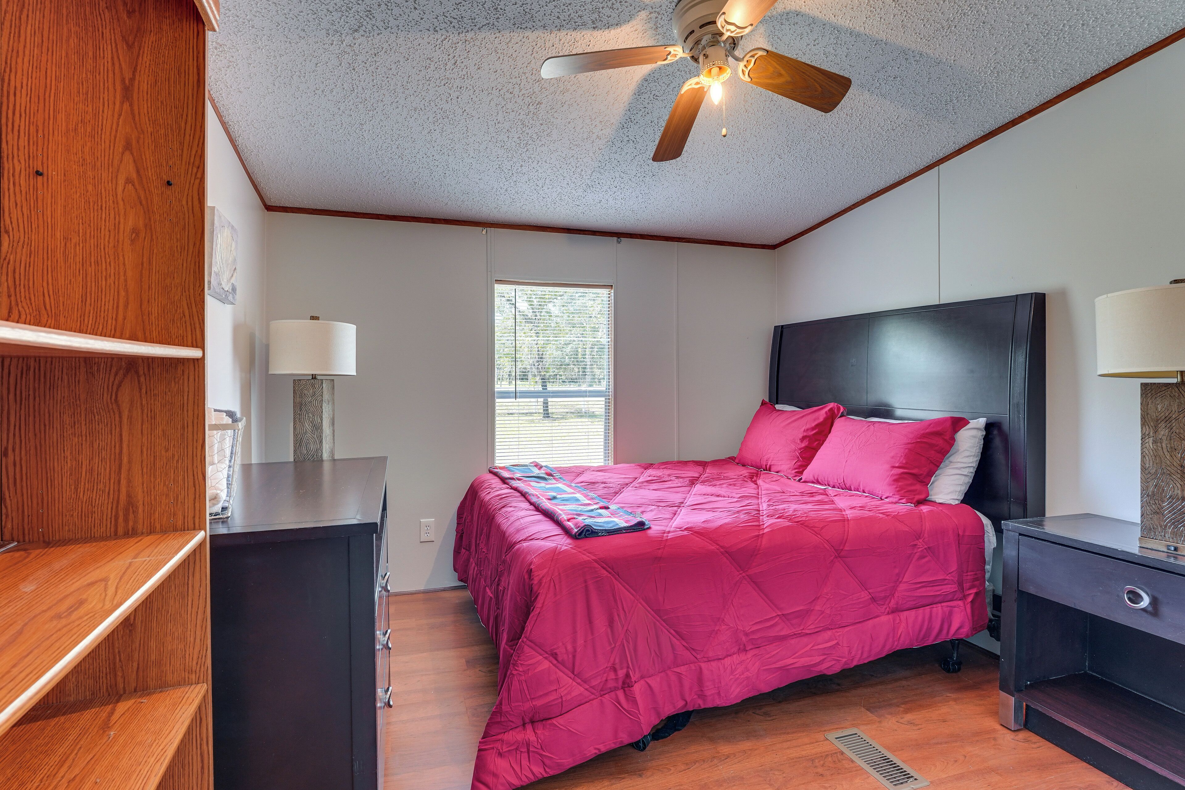 Une chambre à coucher comprenant un lit, des tables de chevet, un ventilateur de plafond, une fenêtre et une étagère en bois.