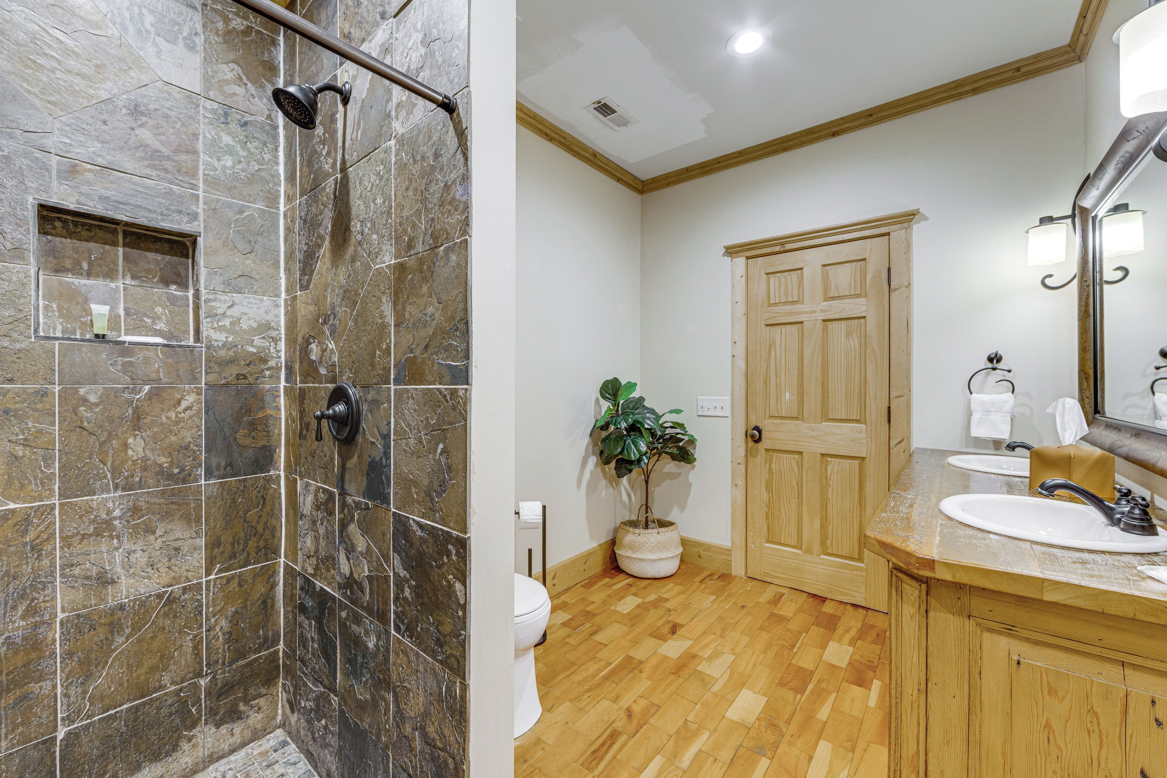 A bathroom with a shower, toilet, sink, and wooden cabinets.