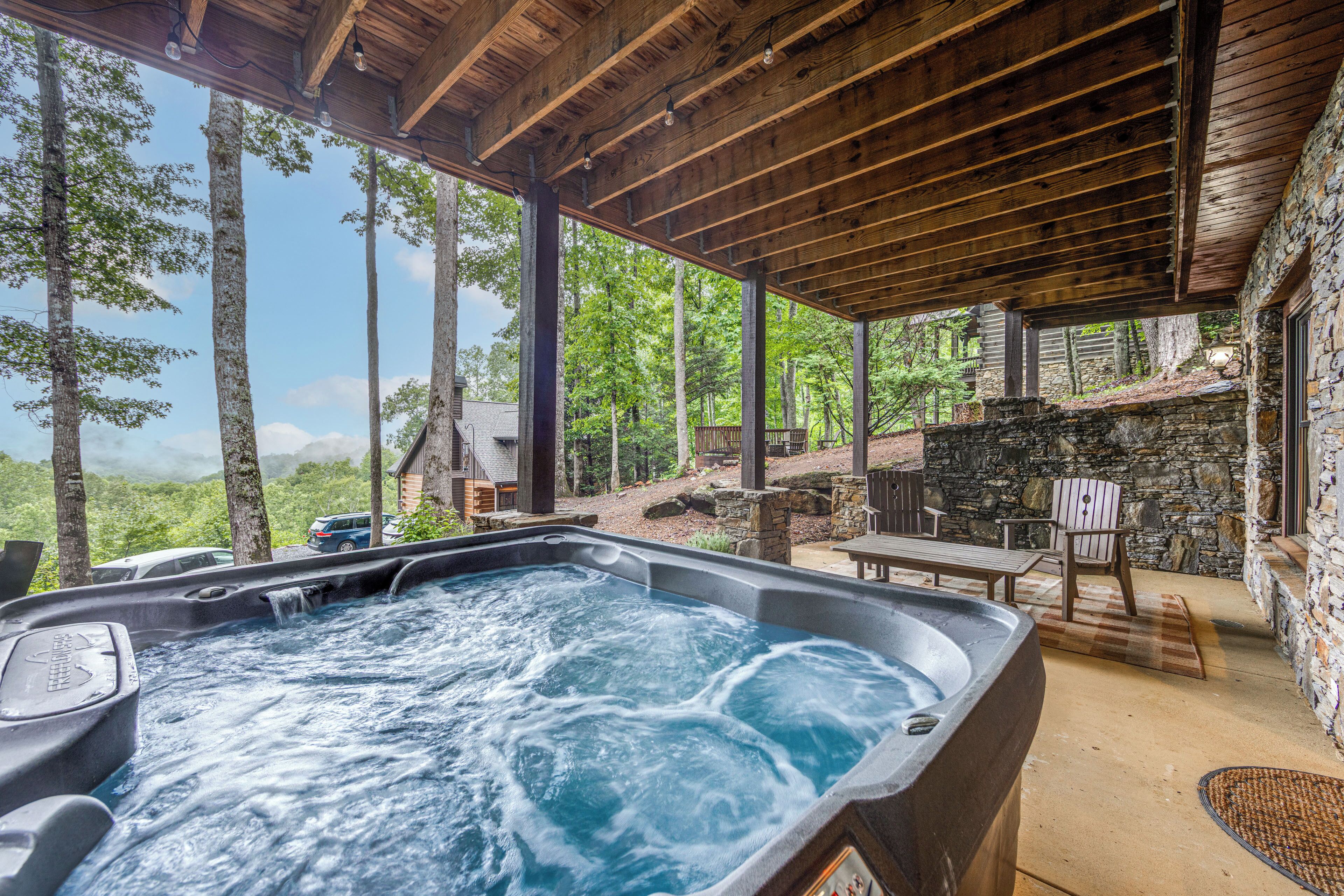 A hot tub with a stone wall backdrop, wooden deck, and outdoor seating.