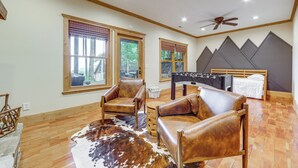 A room with a wooden floor, leather chairs, a foosball table, a bed, and large windows. - Franklin Cabin w/ Hot Tub, Theater & Fire Pit! (Franklin)