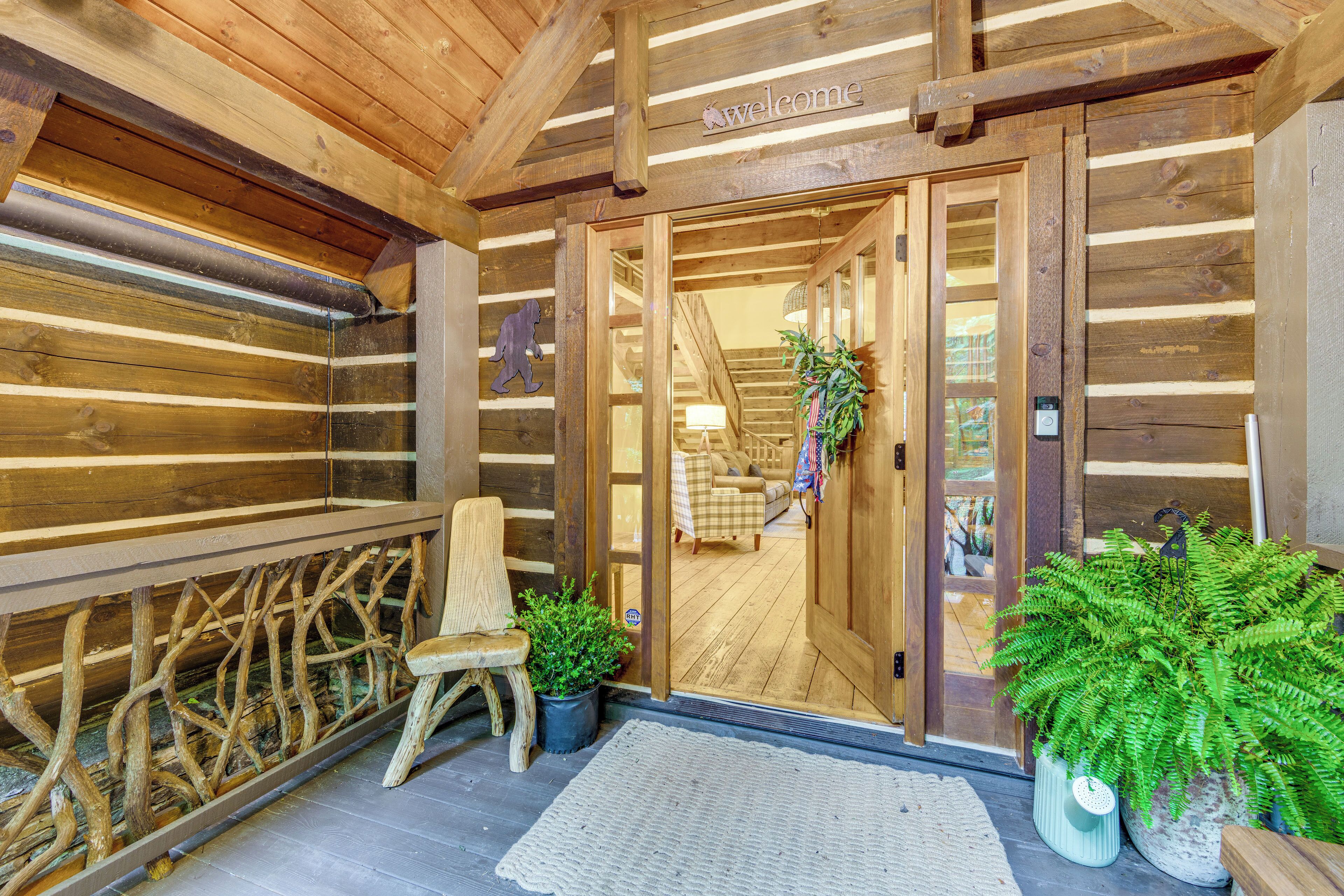 L’entrée d’un chalet en bois, avec une pancarte indiquant « Bienvenue », un banc et des plantes en pot.