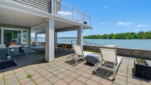 Un patio cubierto con mobiliario exterior, una parrilla y vistas a un lago.