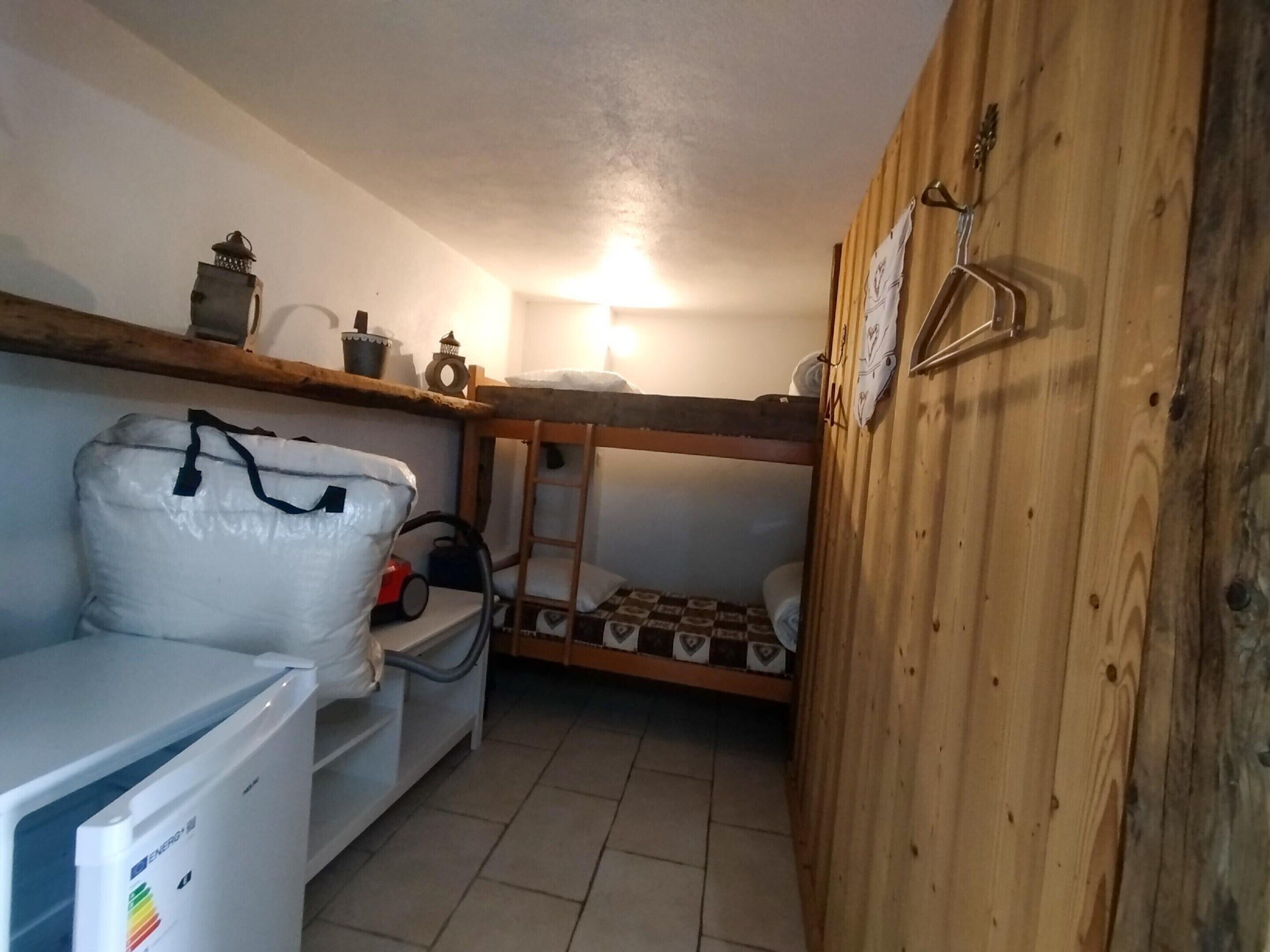 Habitació petita amb un llit superposat, un sofà blanc, un radiador i una petita estant amb objectes decoratius.