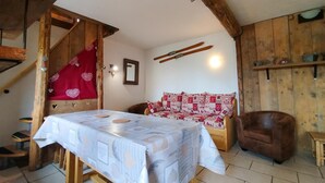 A rustic room with a wooden staircase, a sofa with patterned cushions, a table with a tablecloth, and a wooden wall with shelves. - Chalet Magui, Saint-sorlin-d\"arves (Saint-Sorlin-d'Arves)