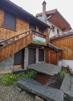 A wooden building with a balcony, stone steps, and a sign indicating a location. - Chalet Magui - 3P8 (Saint-Sorlin-d'Arves)