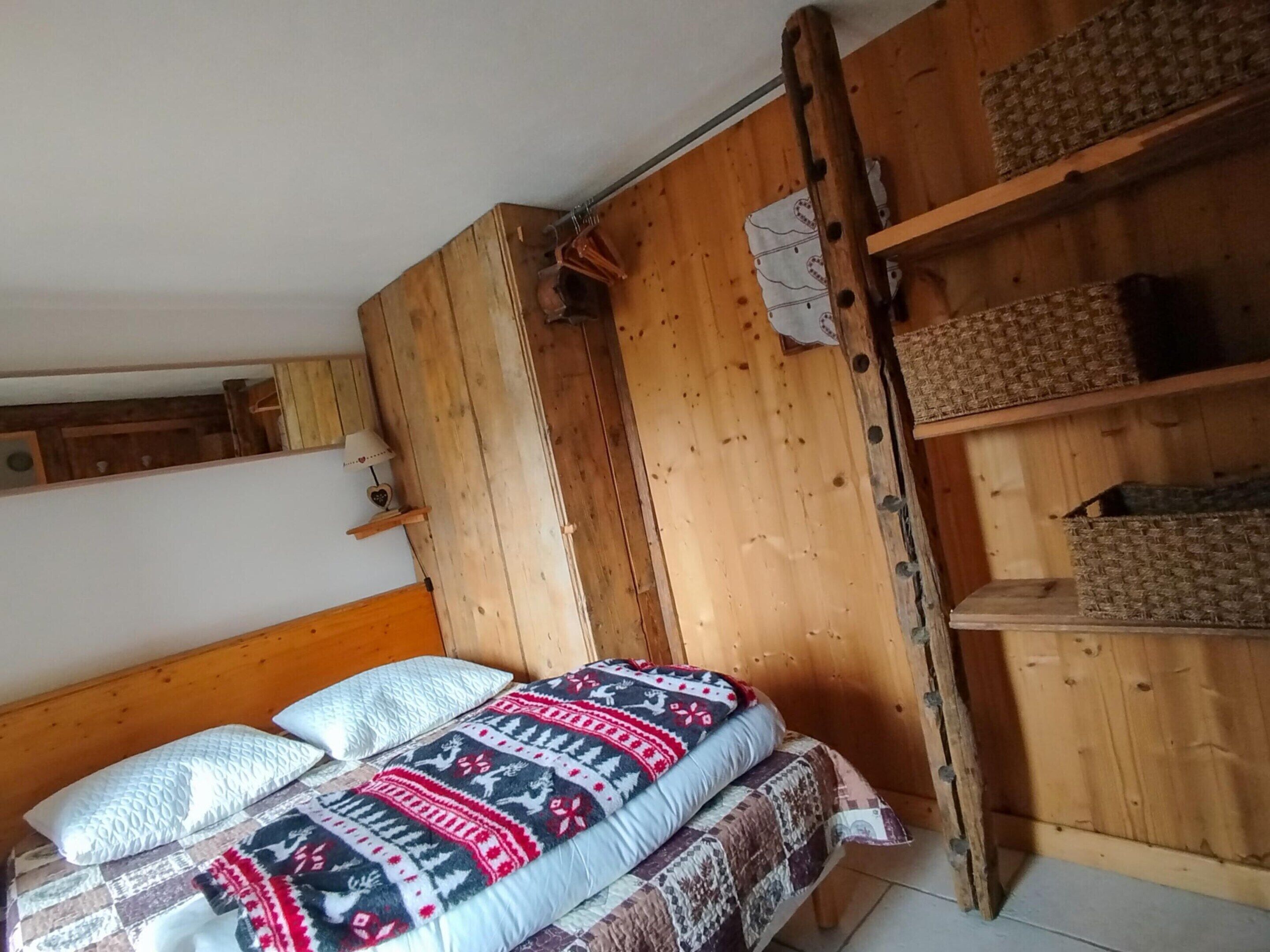 A wooden bed with patterned bedding, a shelf with baskets, and a wooden wall.