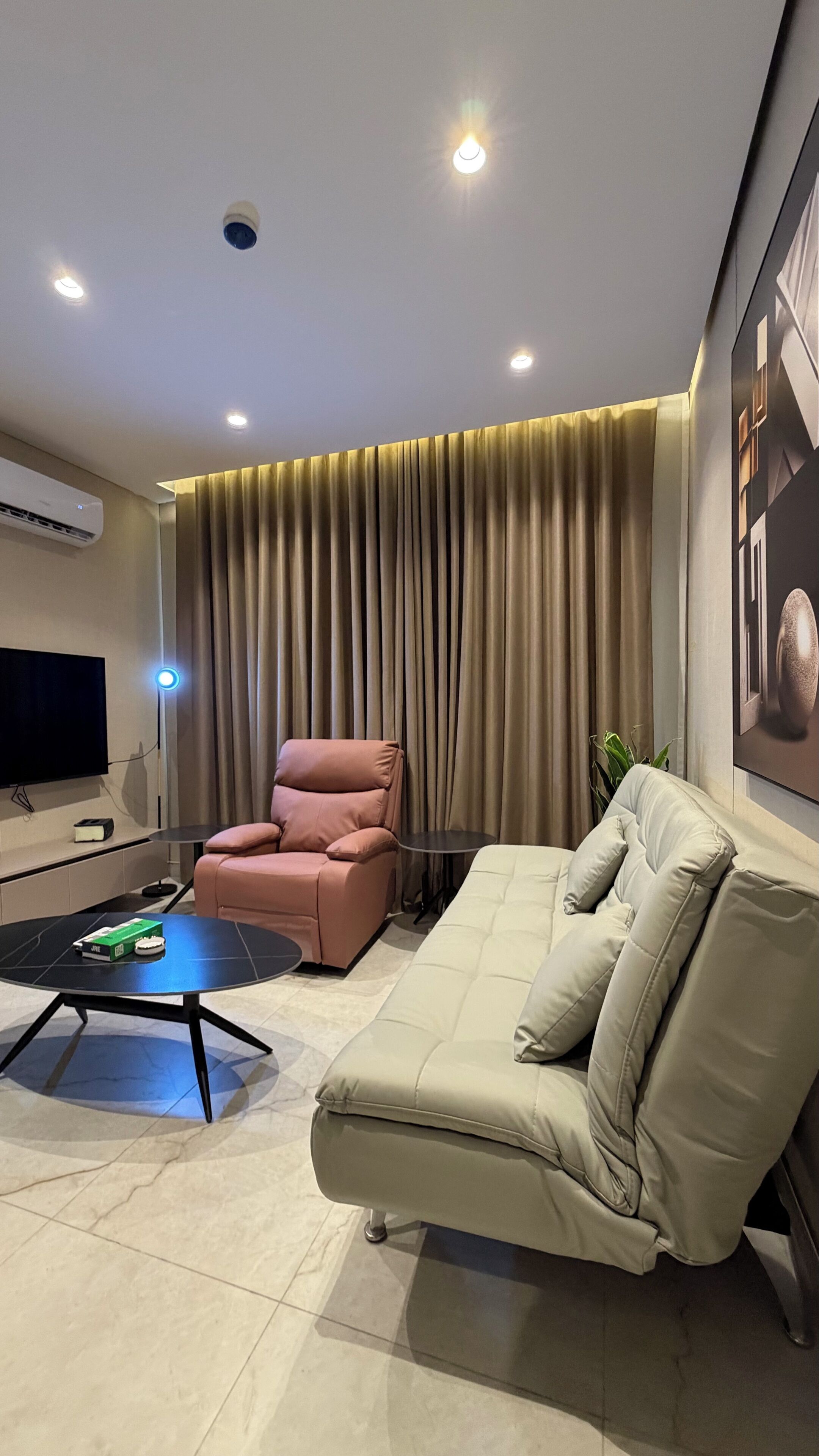 A modern living room with a sofa, a pink chair, a TV, and a wall-mounted air conditioner.