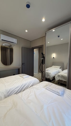 Quarto de hotel com duas camas, um aparelho de ar condicionado, um espelho e uma porta que dá para outro quarto.