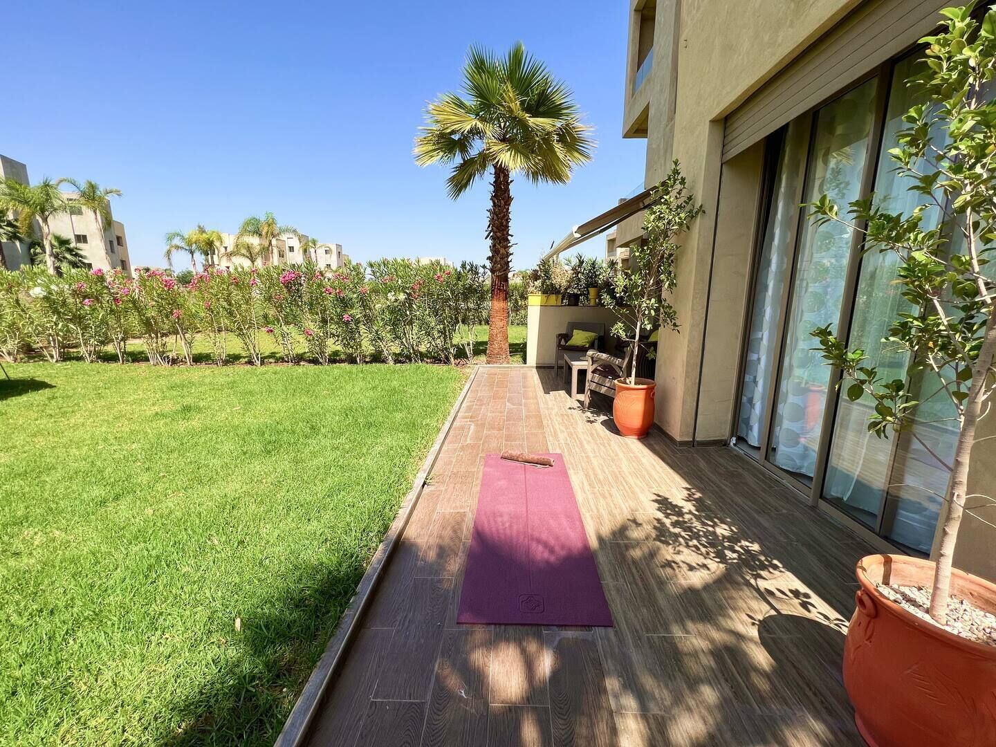 A patio with a wooden deck, a purple yoga mat, a palm tree, and potted plants.