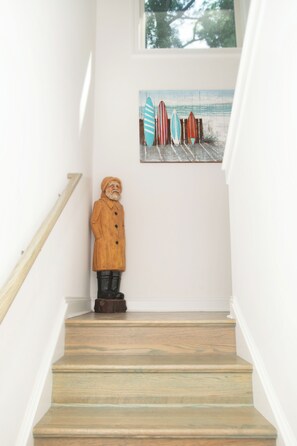 Eine Treppe mit hölzernem Geländer, einer Holzstatue und einem Meeresblick-Gemälde an der Wand.