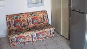 A kitchen with a patterned sofa, a refrigerator, a door with a glass panel, and a tiled floor. - Les Sables D'or Ndeg28 - 2P6 (Agde)