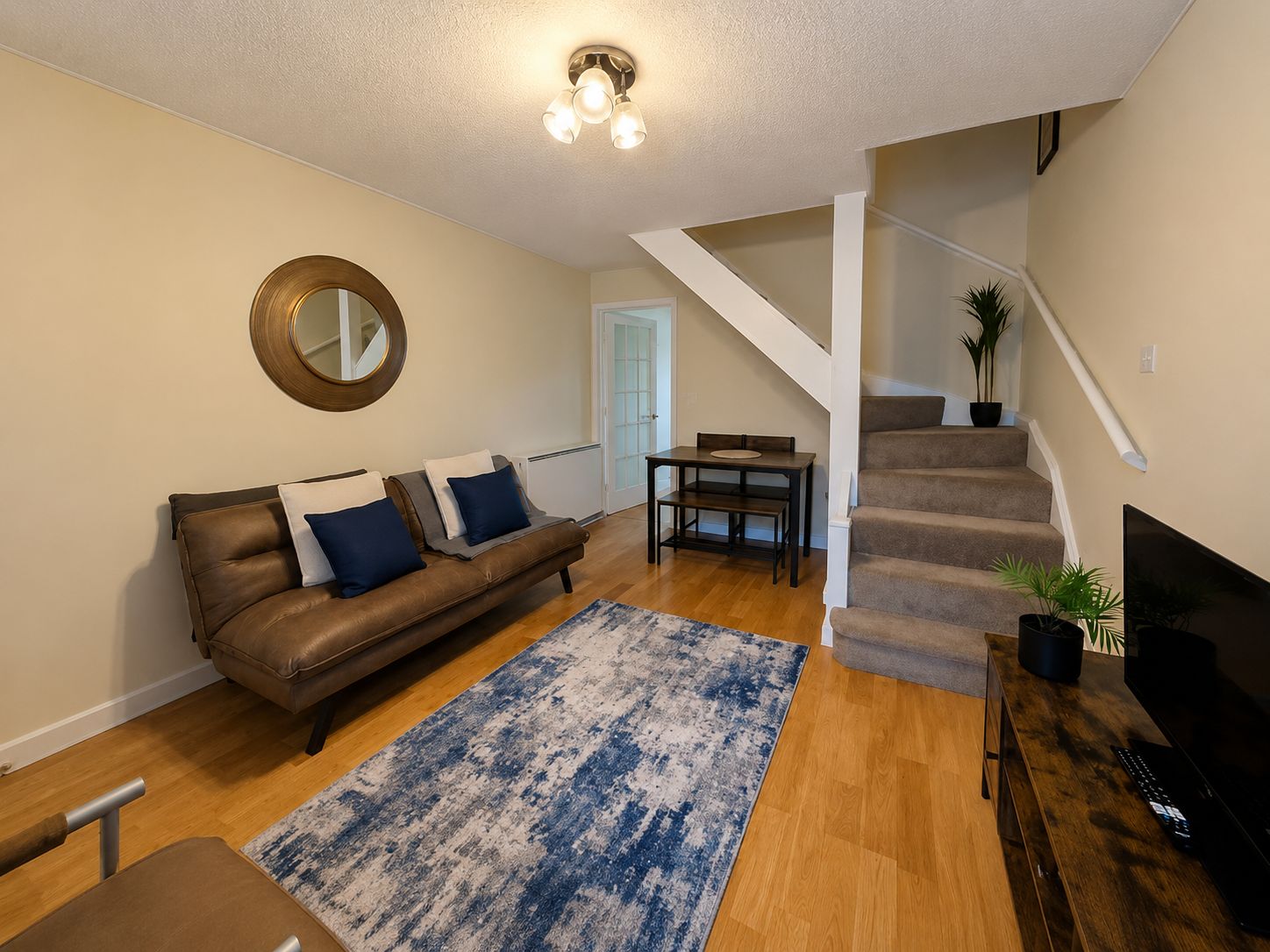 A living room with a brown leather sofa, a coffee table, a blue patterned rug, a television, and a staircase leading to another level.