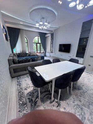 Un salon moderne comprenant un canapé, une table à manger et des chaises, un téléviseur à écran plat et un luminaire décoratif au plafond.
